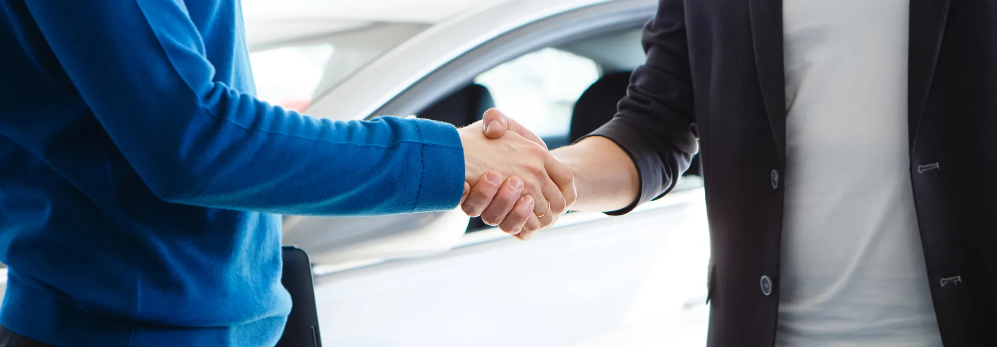 Handshake between a salesperson and a customer in front of a car